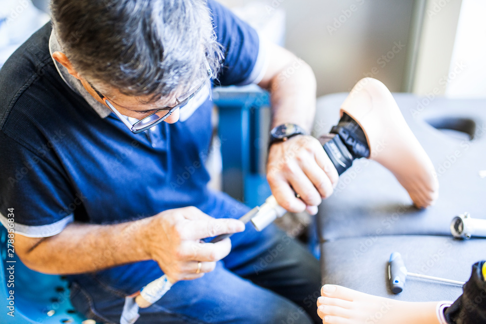 Prosthetic engineer reviewing the prosthesis of a patient and improving the material in his workshop Prosthetic engineer reviewing the prosthesis of a patient and improving the material in his workshop