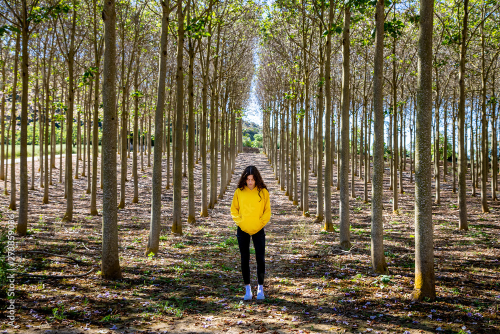 Beautiful young female with long black hair standing in yellow sweatshirt on nature background and looking down Beautiful young female with long black hair standing in yellow sweatshirt on nature background and looking down