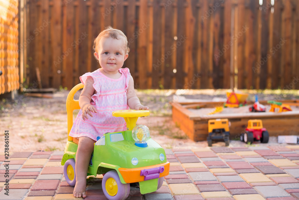 Fototapeta premium Baby girl driving a toy car at the playground outdoor, summer background, copy space