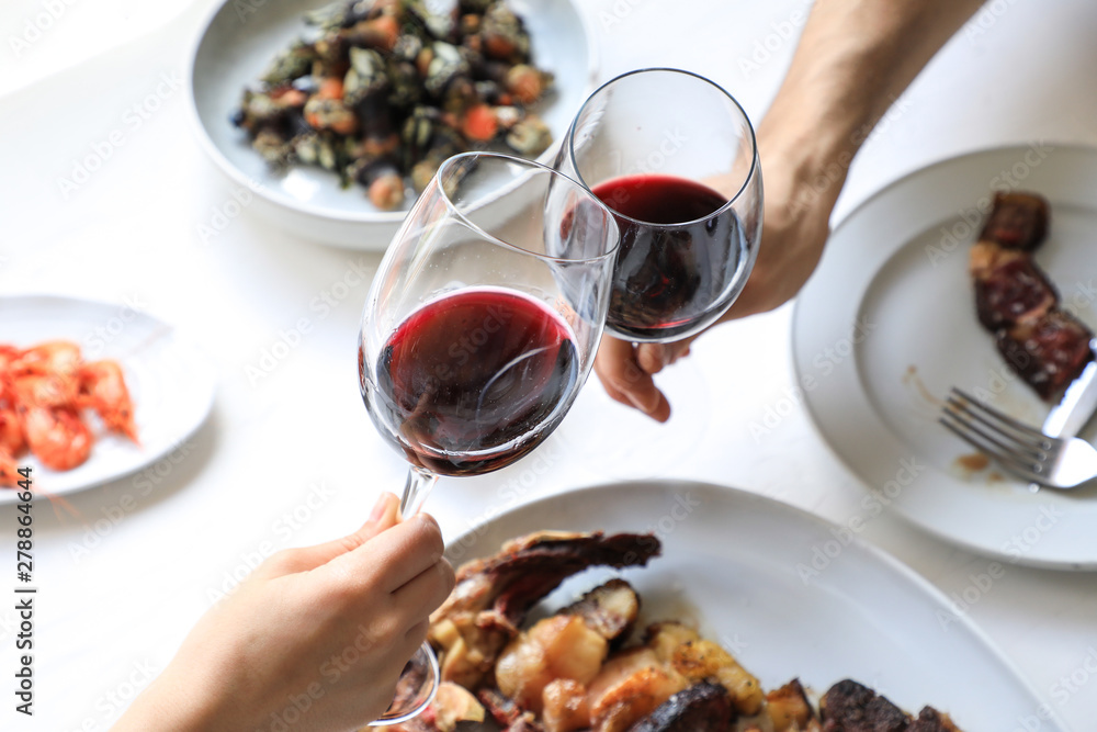 From above crop hands of people clinking with wine glasses while eating delicious meal on white background From above crop hands of people clinking with wine glasses while eating delicious meal on white background