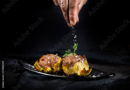 Crop hand of person sprinkling tasty stuffed artichokes with salt on black background photo