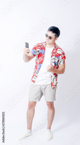 A Portrait of young tourist asian man wearing floral shirt and showing gesture sign. or laptop, Smartphone, camera and wallet stand in isolated background