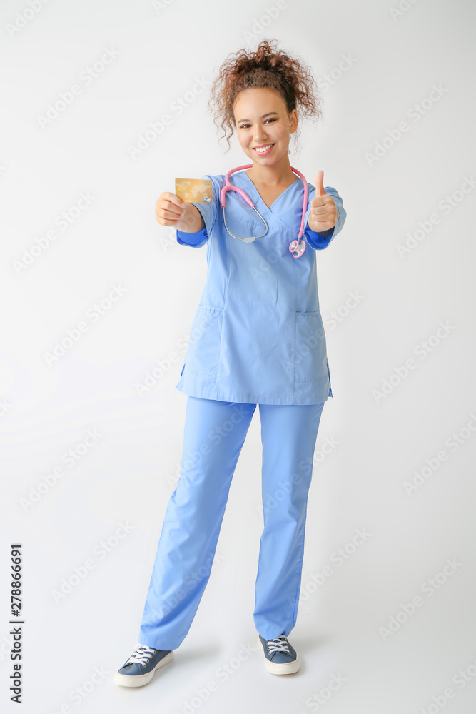 African-American doctor with credit card showing thumb-up on light background African-American doctor with credit card showing thumb-up on light background