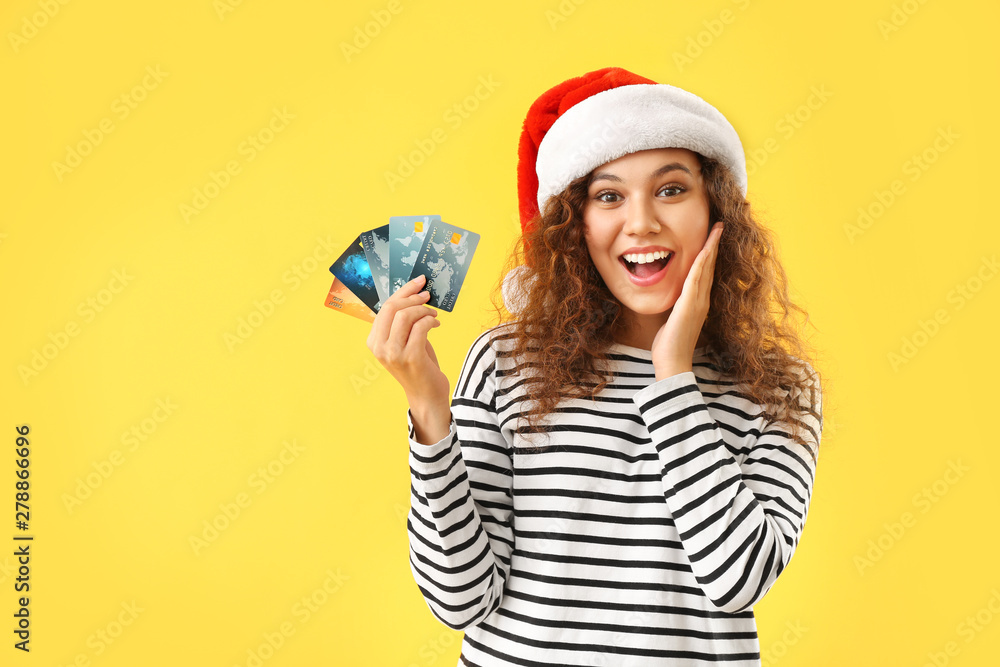 Happy African-American woman in Santa hat and with credit cards on color background Happy African-American woman in Santa hat and with credit cards on color background