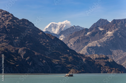 A fishing boat sailing in Alaska with huge mountains and snowy peak in the background