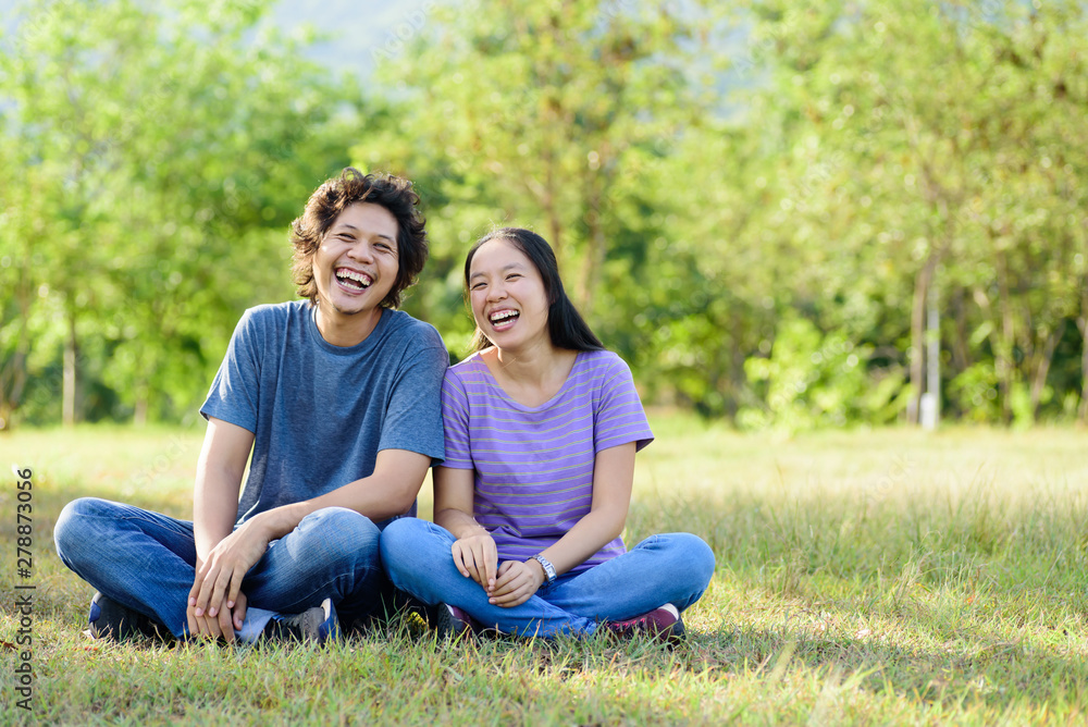 Happy Asian couple sitting and laughing on green grass in outdoor