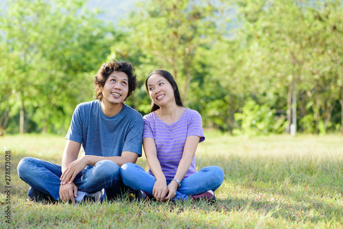 Happy Asian couple sitting on green grass in outdoor