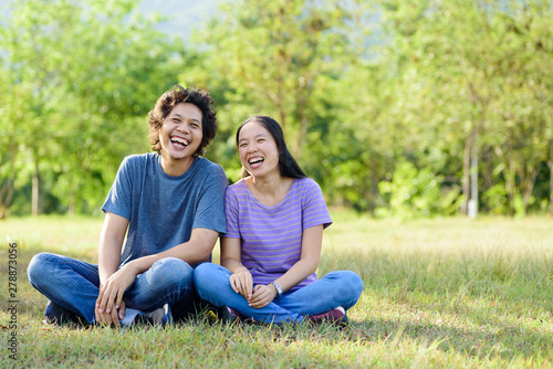 Happy Asian couple sitting and laughing on green grass in outdoor