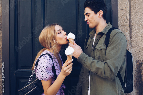 Cheerful young attractive woman and boyfriend eating cornet of ice cream outdoors