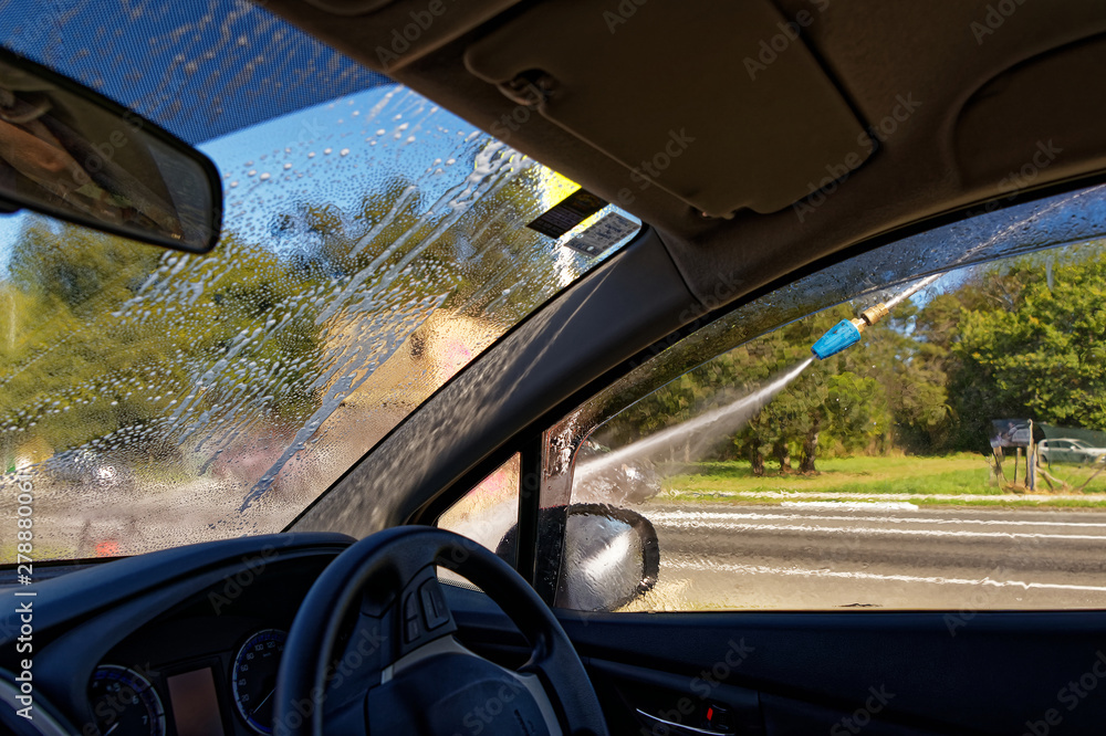 A car is being hand washed, the hose can be seen outside the driver's window A car is being hand washed, the hose can be seen outside the driver's window