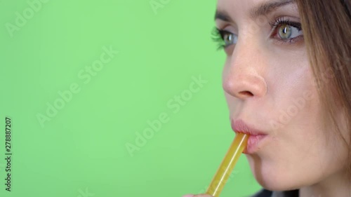 Extreme close up tracking shot of young woman with green eyes drinking freshly squeezed juice using drinking straw photo