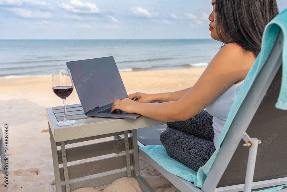 Asian woman using laptop with glass of red wine on table