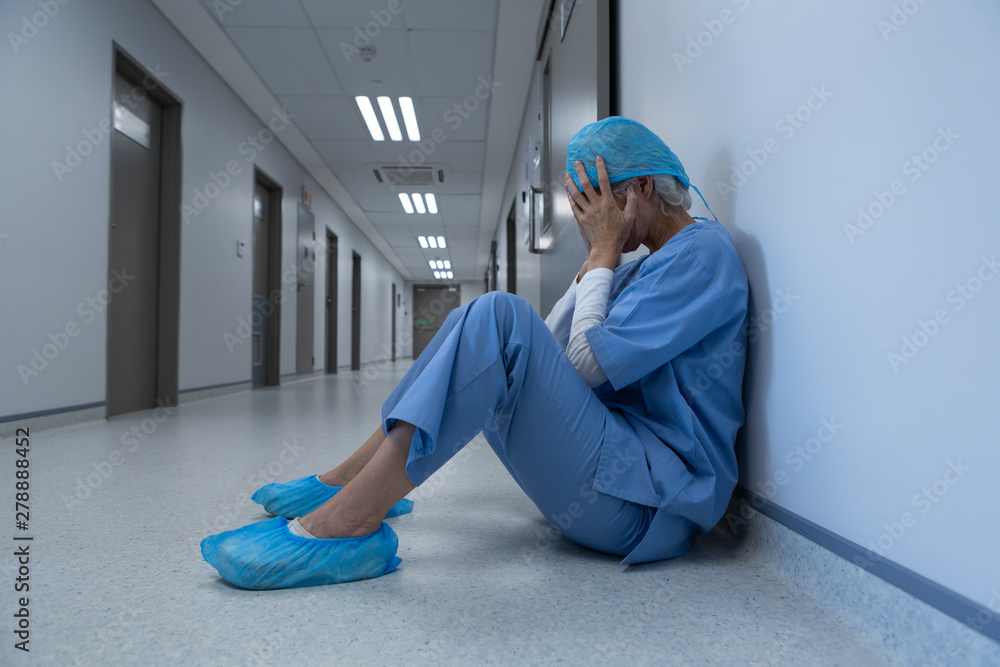 Tensed female surgeon covering her face in the corridor of hospital Tensed female surgeon covering her face in the corridor of hospital
