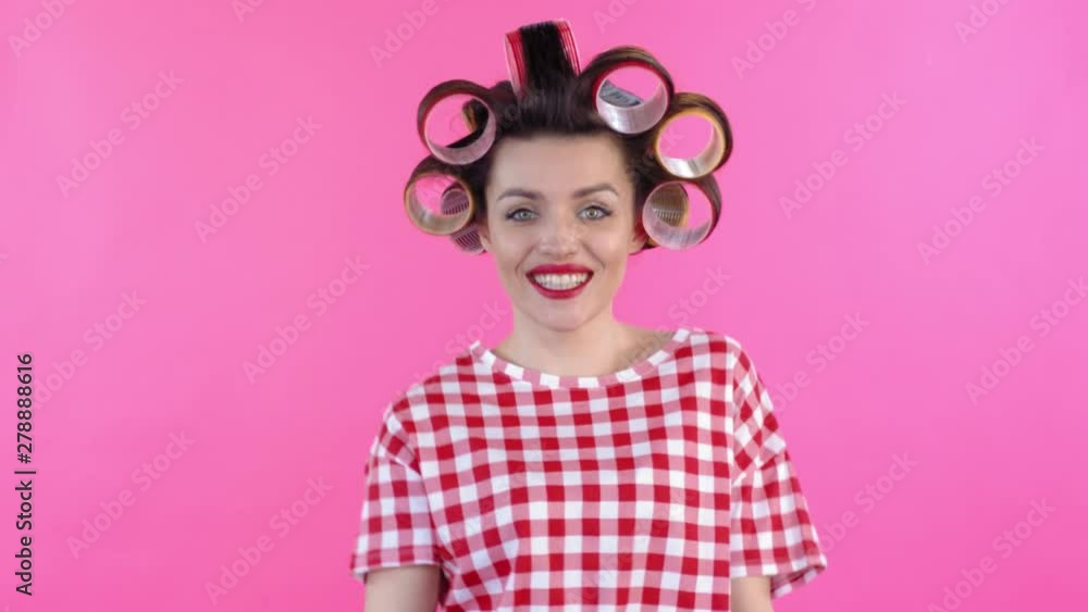 Medium shot of playful woman wearing hair rollers, making crazy faces and smiling at camera when dancing isolated on pink background Medium shot of playful woman wearing hair rollers, making crazy faces and smiling at camera when dancing isolated on pink background