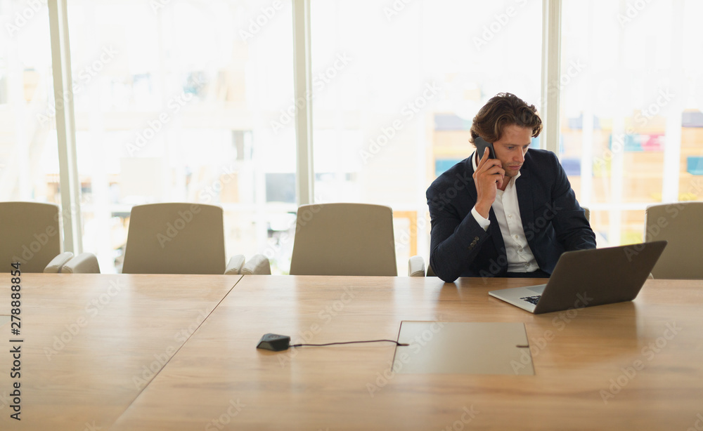 Businessman talking on mobile phone while using laptop in the conference room Businessman talking on mobile phone while using laptop in the conference room