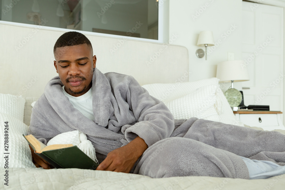 Man reading a book while lying on bed in bedroom at comfortable home