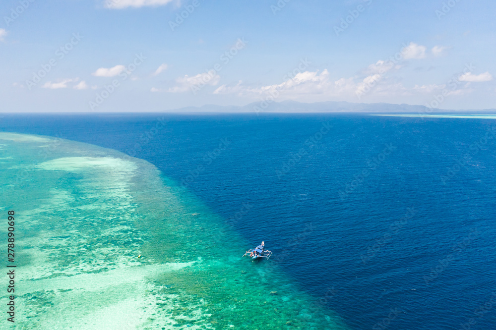 Large coral reef, top view. Tourist boat near the atoll. Seascape in the Philippines in sunny weather.