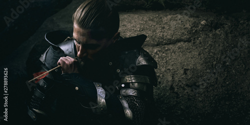 Mystery scarface knight in armor with sword and crossbow in the forest