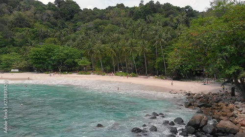 Aerial drone view of beautiful exotic white sand beach, volcanic stones and clear turquoise sea water in Thailand. Paradise beach. Green rainforest with coconut palm trees.
