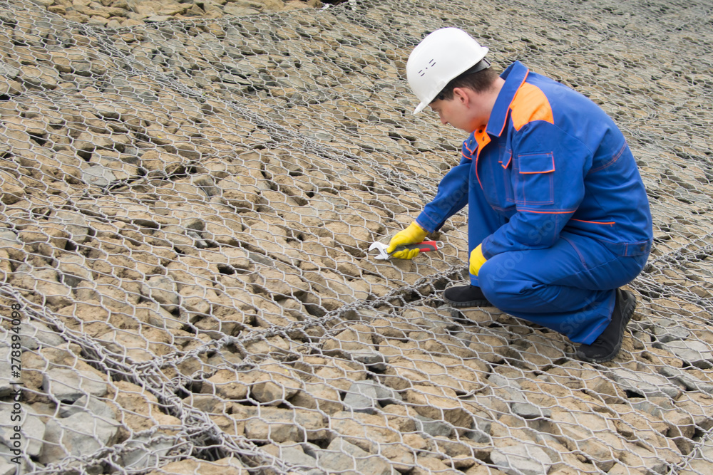 worker in blue uniform and white helmet repairing a grid for ground stones worker in blue uniform and white helmet repairing a grid for ground stones