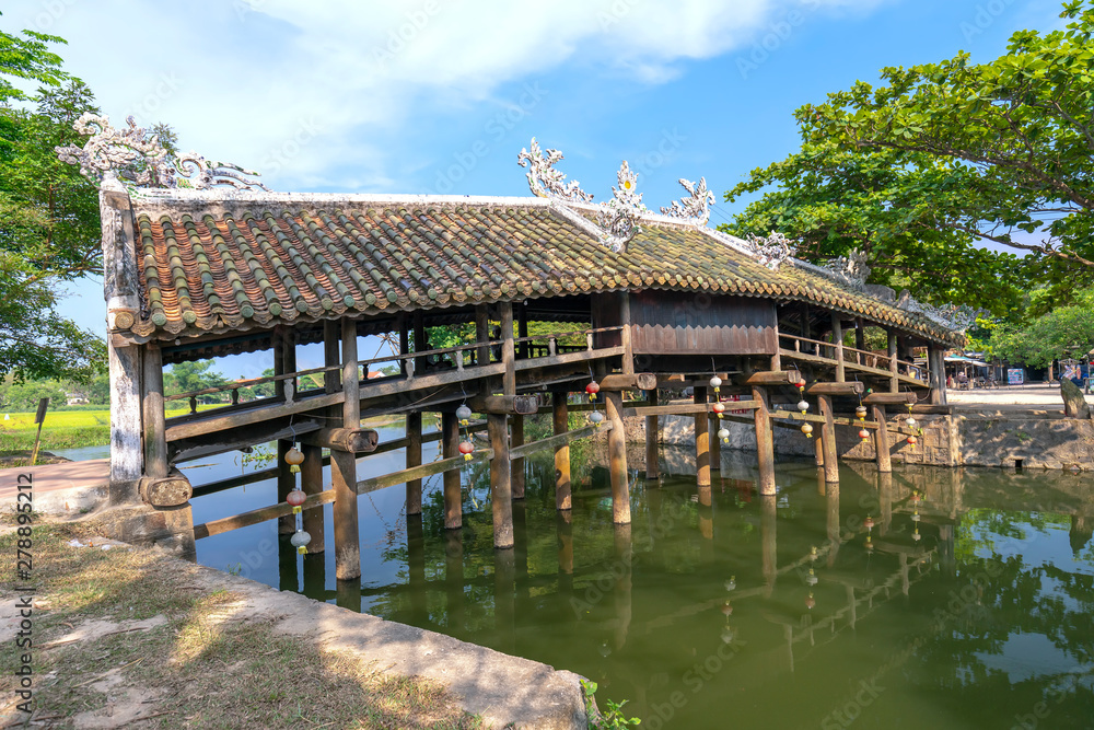 Old wooden bridge crosses the river branch decorated with an upper tile roof dating from the 19th century near Hue city, Vietnam.