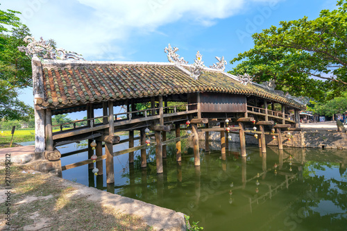 Old wooden bridge crosses the river branch decorated with an upper tile roof dating from the 19th century near Hue city, Vietnam.