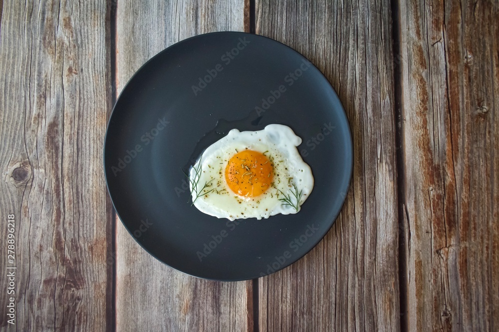 Fried eggs on a black round plate with greens on a brown wooden background Fried eggs on a black round plate with greens on a brown wooden background