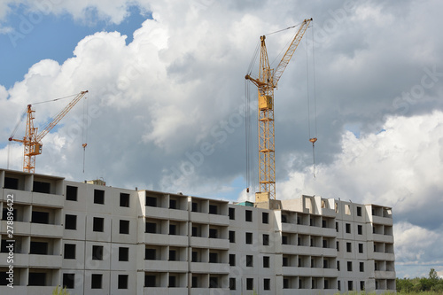 Yellow cranes and the construction of prefabricated houses on a background of blue cloudy sky. Building