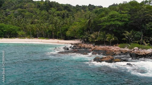 Aerial drone view of beautiful exotic white sand beach, volcanic stones and clear turquoise sea water in Thailand. Paradise beach. Green rainforest with coconut palm trees.
