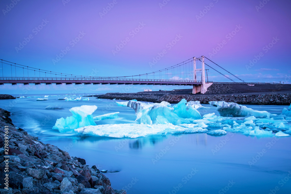 Fototapeta premium Iceberg parts float to the ocean under a bridge in the bay in the famous Jokulsarlon ice lagoon in Iceland. (global warming, greenhouse effect - concept)