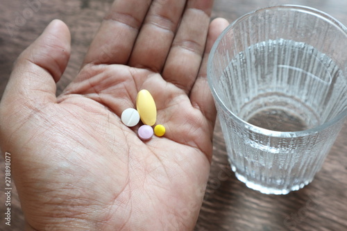 medicine on hand and glass of water on wooden background.
