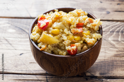 Pilaf with vegetables and chicken in wooden bowl on wooden background.