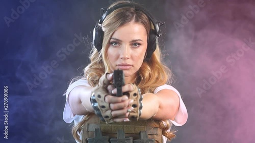 Special Troops woman soldier in military uniform and protective headphones developing her shooting skills over dark smoky background. Beautiful and dangerous. photo