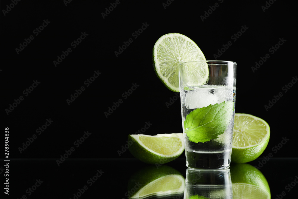 Tequila shot with lime, mint and ice against black background Tequila shot with lime, mint and ice against black background