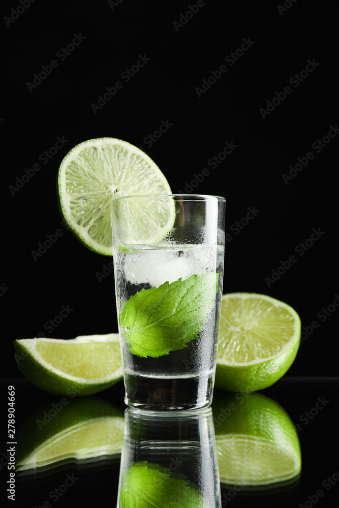 Tequila shot with lime, mint and ice against black background Tequila shot with lime, mint and ice against black background