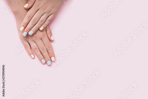 Fresh blue and yellow manicure on pink isolated background. © polinaloves