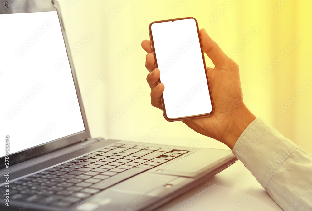 hand with white screen of cellphone and laptop hand with white screen of cellphone and laptop