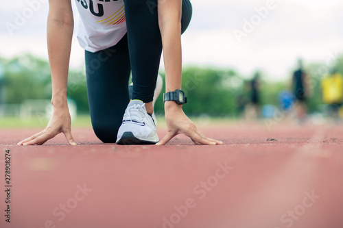 Athlete woman in running start pose on the on racetrack . Sport tight clothes. blurry background. Horizontal