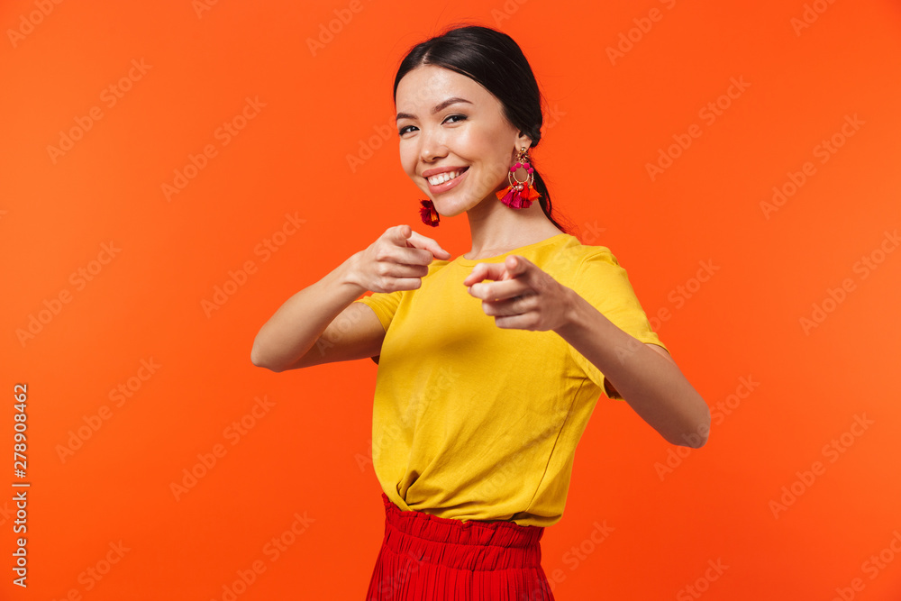 Excited happy young woman posing isolated over orange wall background pointing. Excited happy young woman posing isolated over orange wall background pointing.