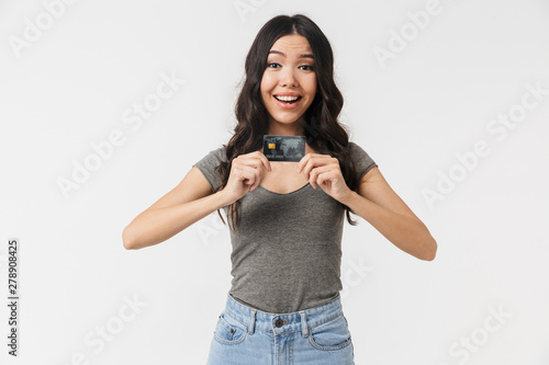 Image of excited brunette woman 20s dressed in basic clothes smiling and holding credit card © Drobot Dean