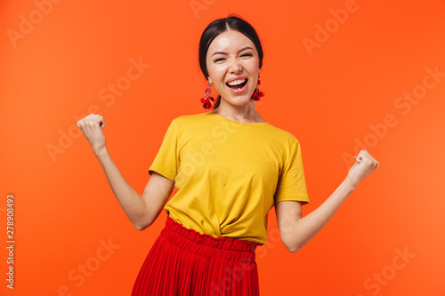 Excited happy young woman posing isolated over orange wall background make winner gesture.