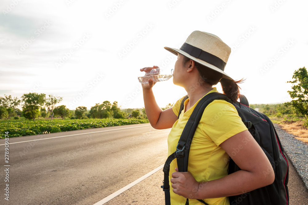 Women backpack tourists, drinking water on the highway, with the golden light of the sun.