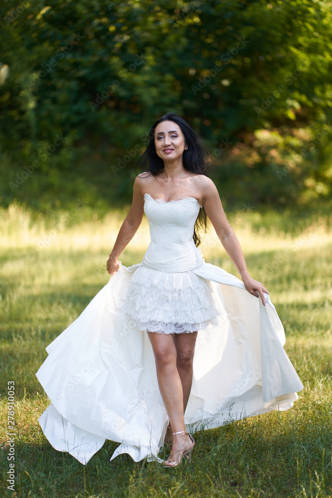 Young pretty brunette smiling woman in white wedding dress, walking outdoors