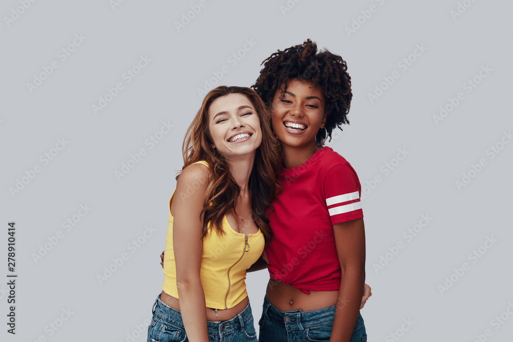Two attractive young women looking at camera and smiling while standing against grey background Two attractive young women looking at camera and smiling while standing against grey background
