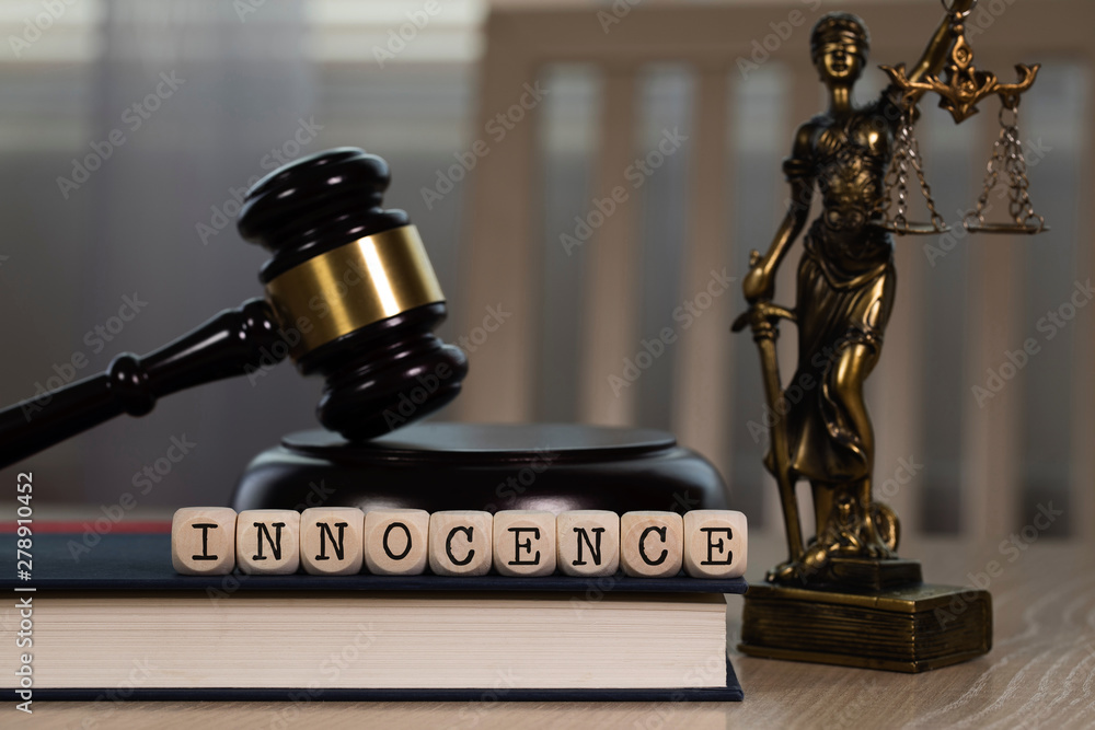 Word INNOCENCE composed of wooden dices. Wooden gavel and statue of Themis in the background.