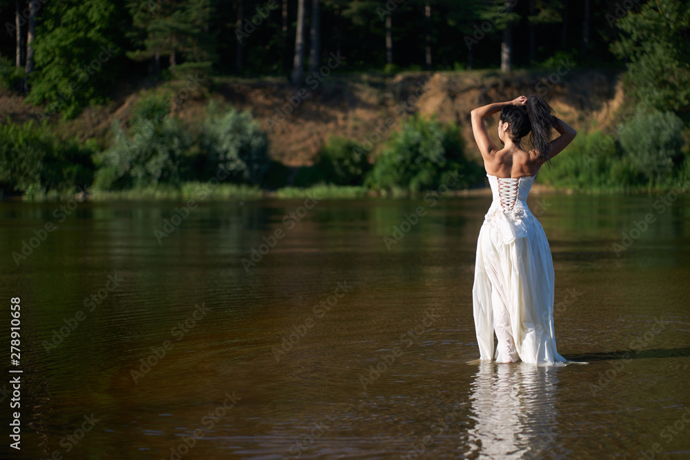 Young pretty brunette woman in white wedding dress walking on the river barefoot, making splashes around Young pretty brunette woman in white wedding dress walking on the river barefoot, making splashes around
