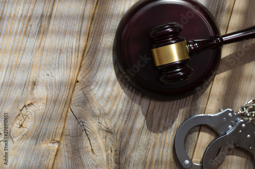 Wooden gavel and handcuff on a wooden surface.