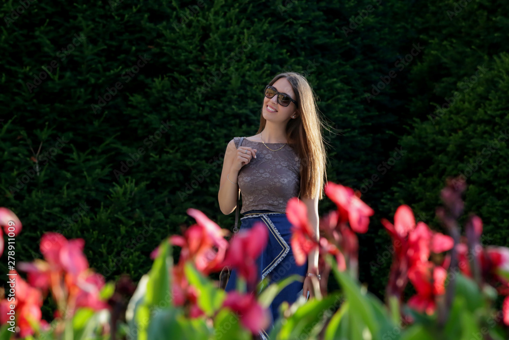 Happy young woman standing in a park near flowers, candid outdoor portrait of beautiful brunette Happy young woman standing in a park near flowers, candid outdoor portrait of beautiful brunette
