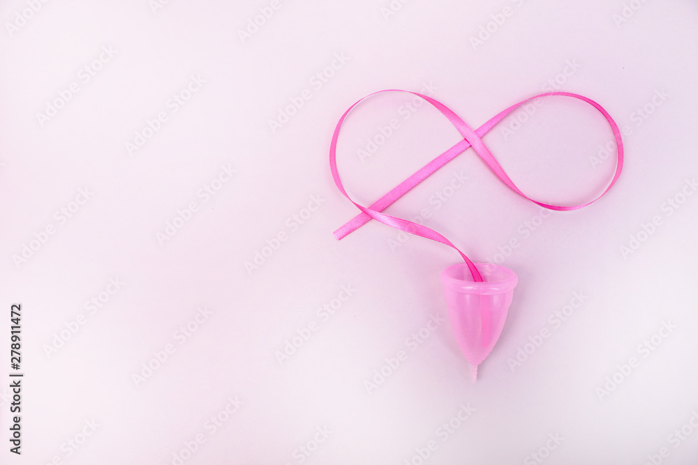A woman holds a menstrual cup in her hand on a pink background. The concept of women's health, hygiene, alternatives pads and tampons