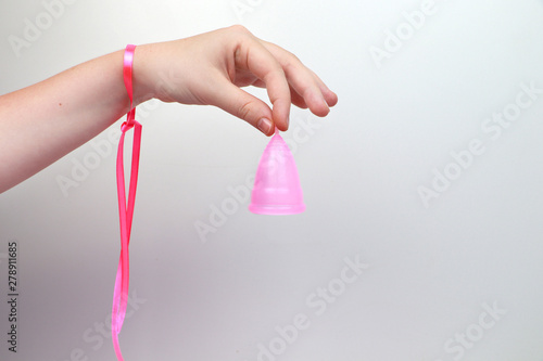 A woman holds a menstrual cup in her hand on a pink background. The concept of women's health, hygiene, alternatives pads and tampons photo